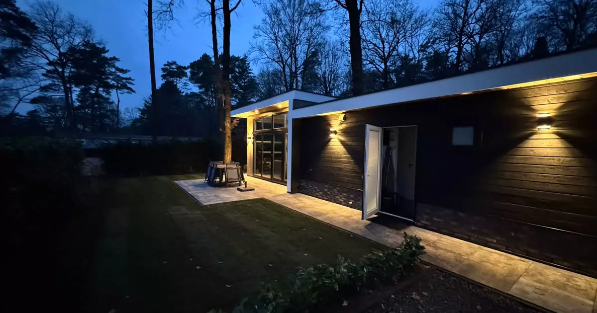 Woeste Hoogte 15 in de schemering, met de buitenlampen aan tussen de bomen