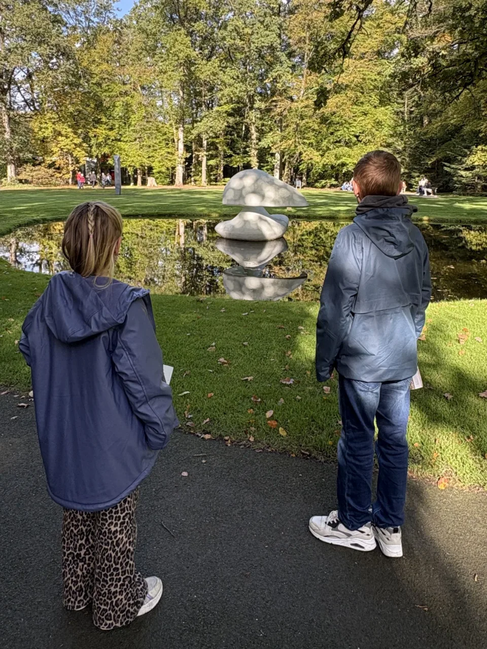 Twee kinderen, van achteren gezien, kijken naar een wit beeld in een vijver in de beeldentuin