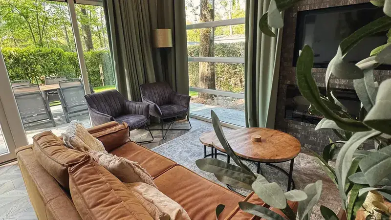 Woonkamer met cognac leren bank, ronde eikenhouten tafels en glazen pui naar de tuin